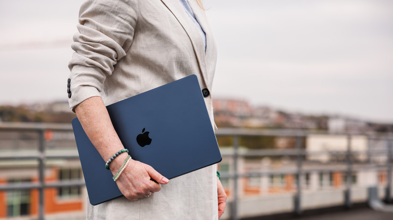 A person walking with a MacBook in hand