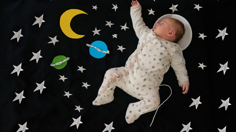 A baby sleeping on a space-themed backdrop.