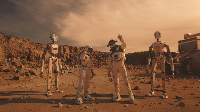 Two astronauts standing on Mars with two robots