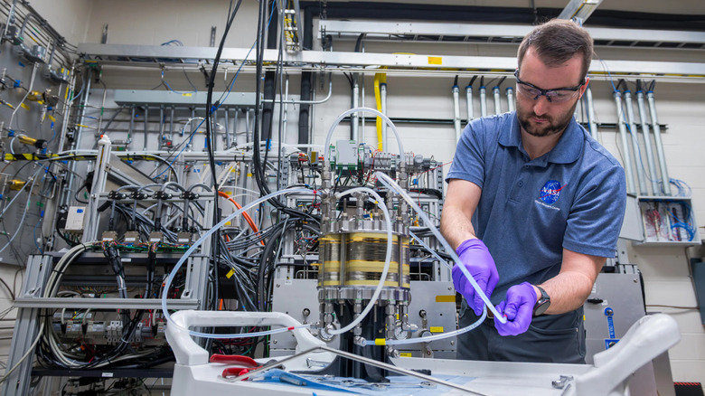 Dr. Kerrigan Cain, in a blue NASA polo and protective glasses, adjusts the tubes of the fuel cell.