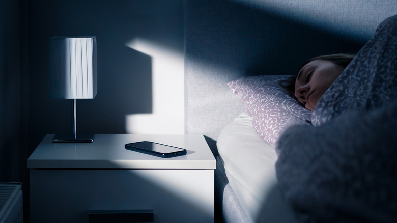 Woman sleeping in bed with phone next to her on nightstand