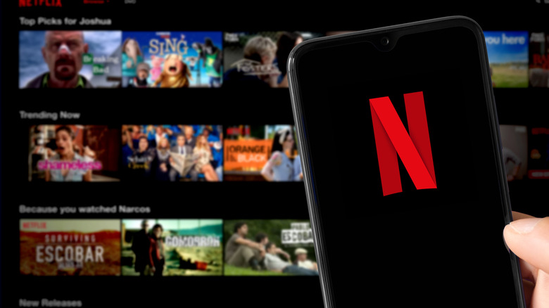 Netflix logo on an iPhone with a smart TV showing the service streaming catalog