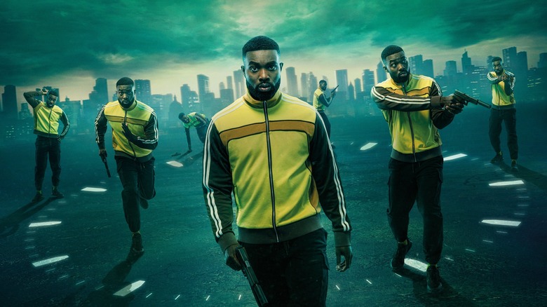Multiple copies of a man in a yellow tracksuit, all of whom are standing on a clock face, with a city in the background. Each copy is performing a differnt action, such as aiming a pistol or running.
