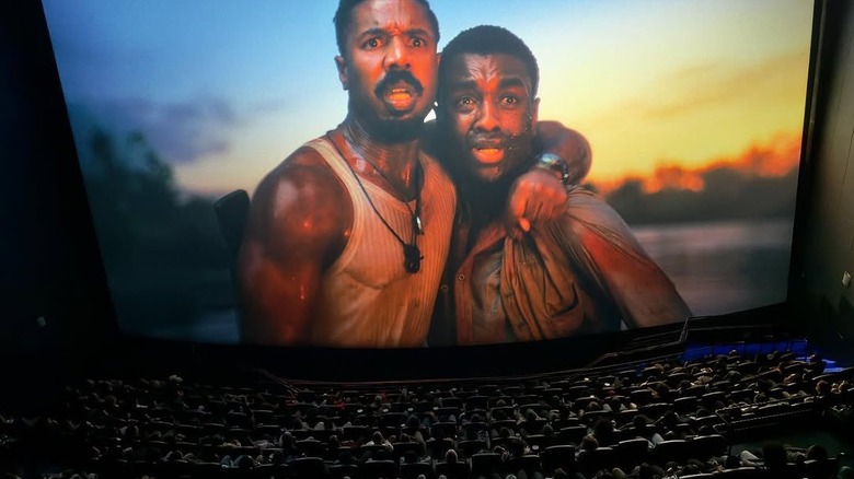 An IMAX screen shows Michael B Jordan and Miles Caton clutching each other against a brilliant sunrise during Warner Bros.'s Sinners.