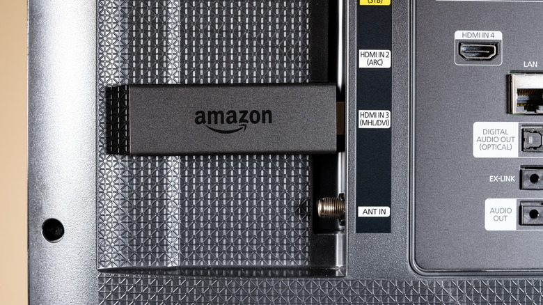 A black Amazon Fire TV Stick plugged into the HDMI input port on the back of a TV.