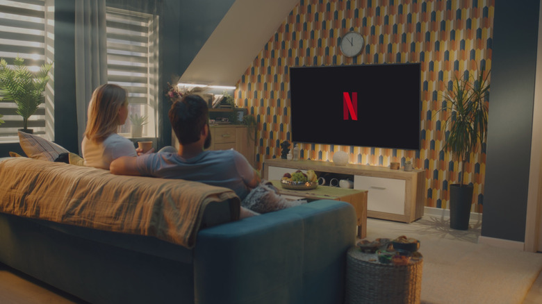Two people on a blue couch watching TV with the Netflix logo on the screen in a colorful living room.