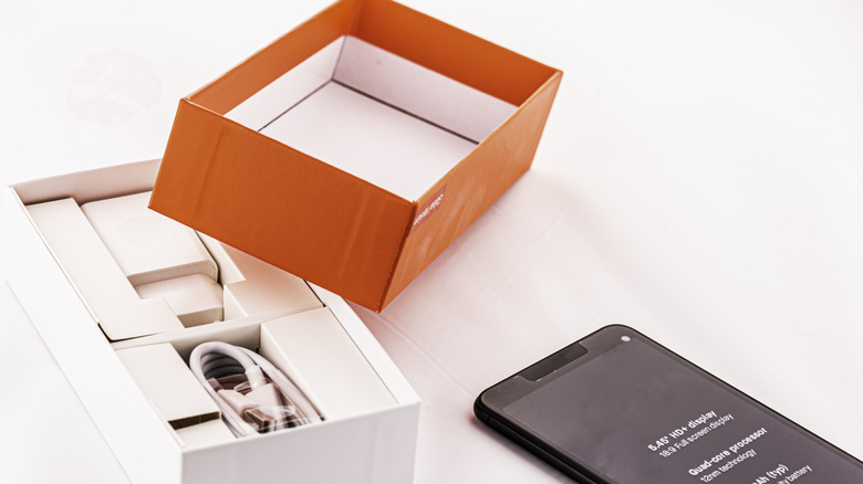 an open smartphone box with cable and adapter with the phone placed next to it