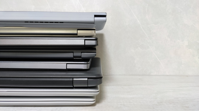 stack of eight laptops on a wooden table against a grey background