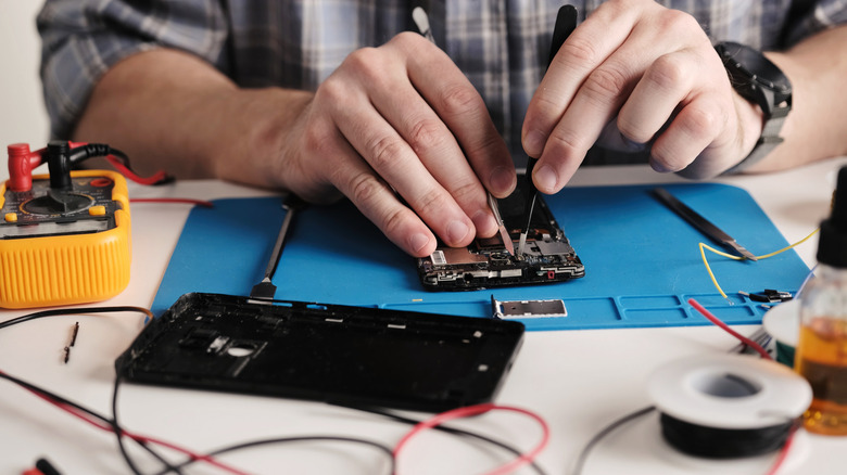 technician inspecting a phone for problems with a multimeter and other tools placed on the desk