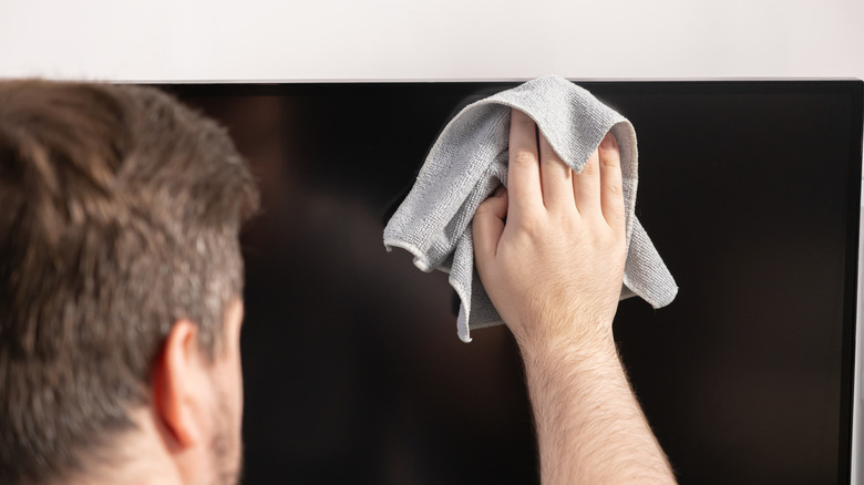 A person cleaning a TV screen with a microfiber cloth