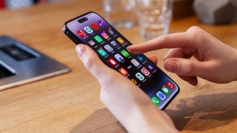 An iPhone in hand with Home Screen showing app icons