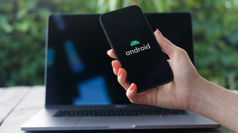 A phone screen showing Android logo and laptop in the background