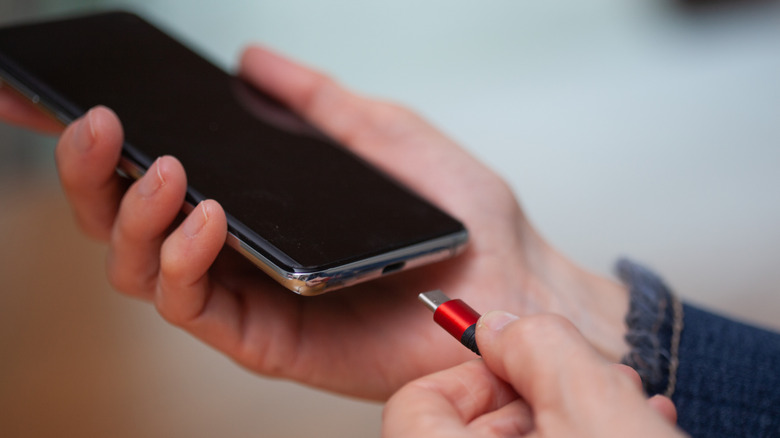 Close up of a man's hands plugging the charge cable into a phone