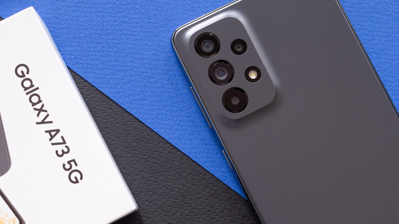 samsung galaxy A73 placed next to its box against a blue and black background