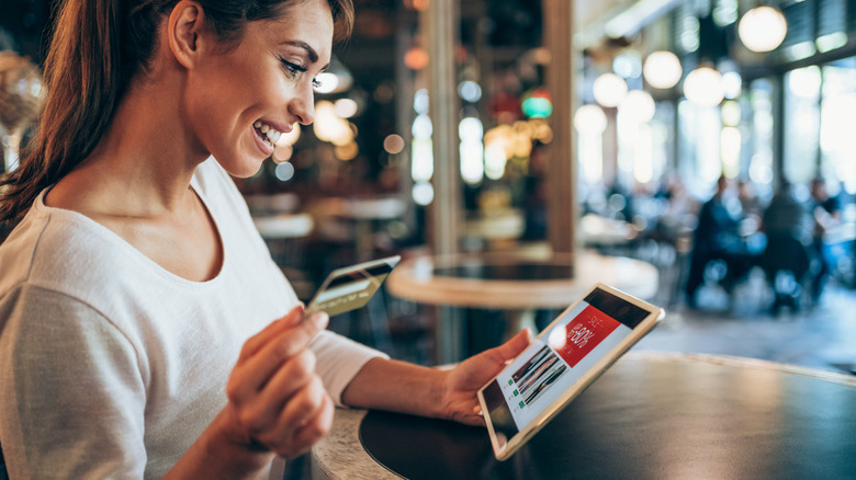 A person completing an online transaction with a credit card on an iPad in a coffee shop.