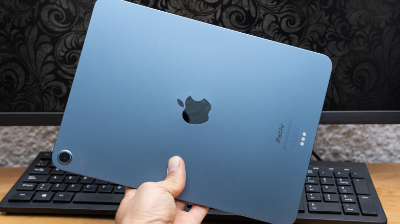 A hand holding an iPad over a desk and keyboard.