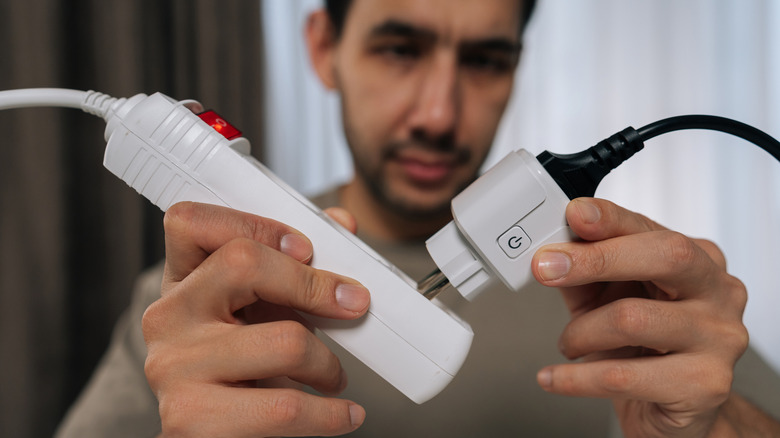 A man plugging a device into a surge protector