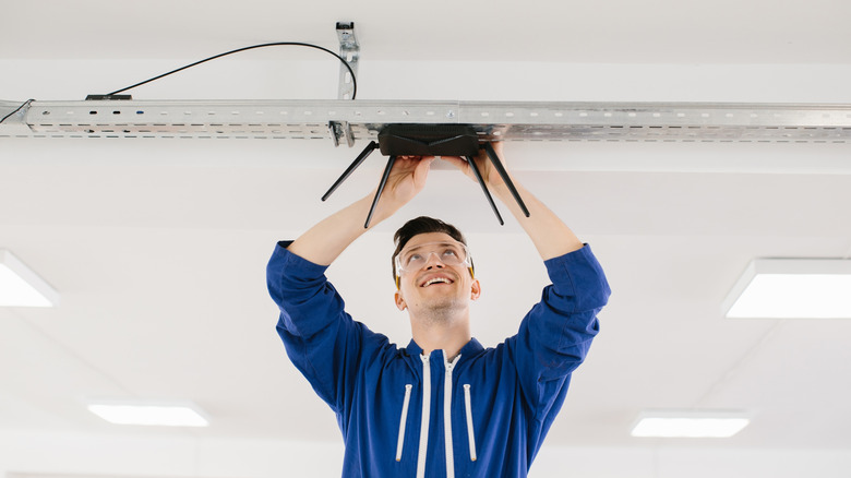 Technician installing a black router in an office ceiling bracket