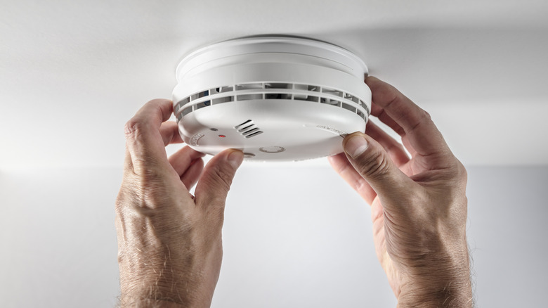 A person inspecting a smoke and fire alarm inside a house