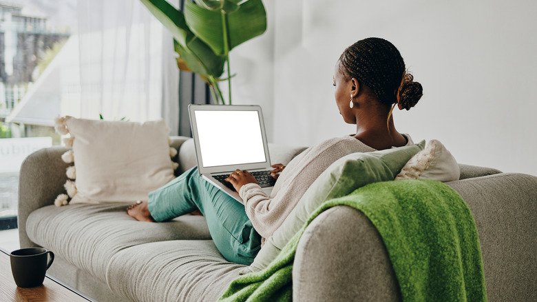 A person with a laptop in their lap while sitting on the couch