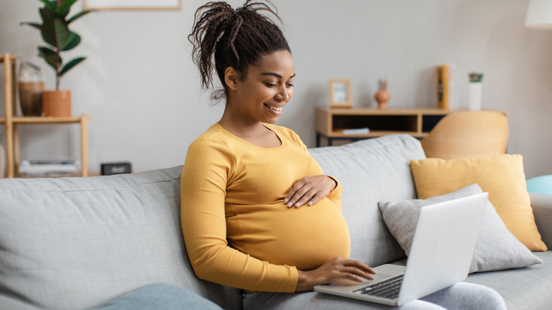 pregnant woman using a laptop on her thighs while sitting on the couch