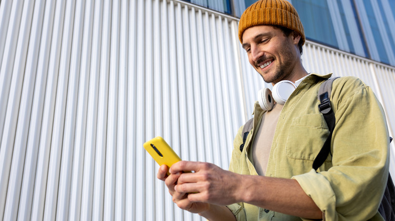 Young man using a smartphone while wearing headphones and a beanie.
