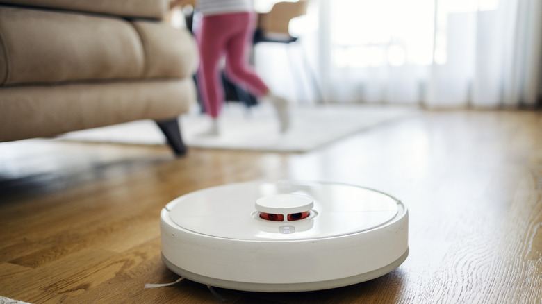 Robot vacuum on a hard floor, person walking in background
