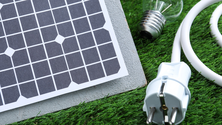 A portable solar panel alongside an electrical plug and light bulb