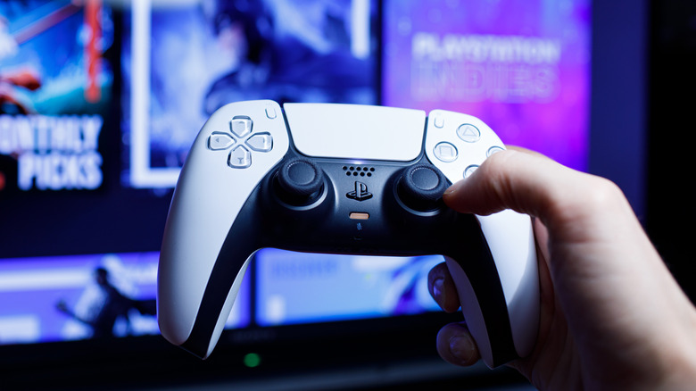 Hand holding PlayStation 5 DualSense controller in front of TV screen