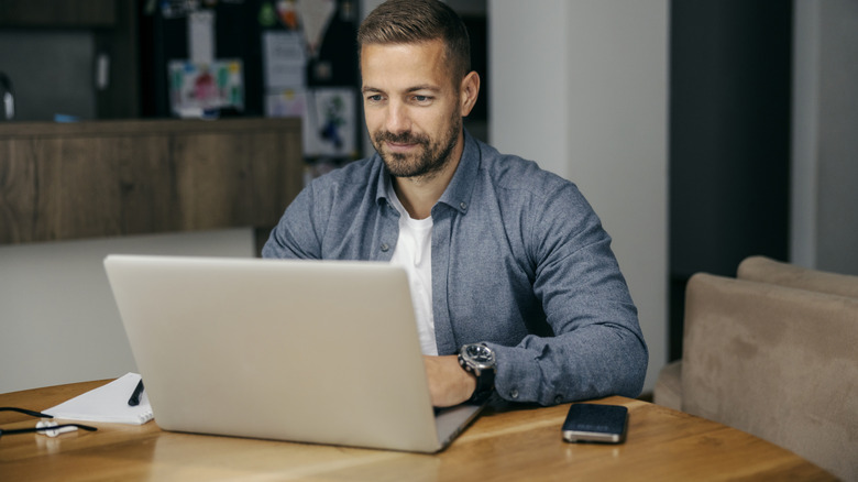 man using unlabeled laptop with a smartphone next to him