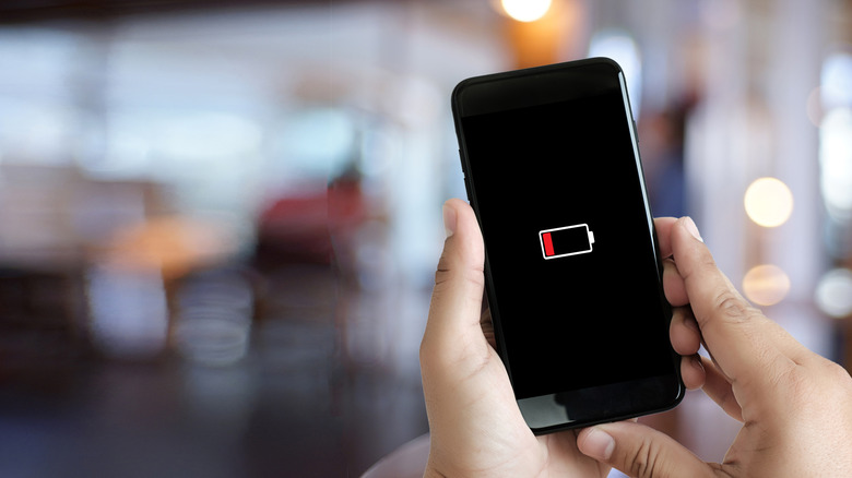 smartphone showing low battery icon, busy background blurred