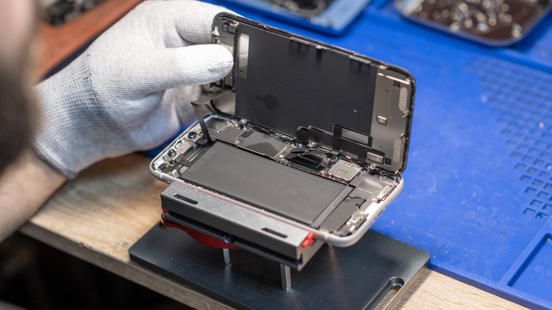 smartphone technician works on replacing a battery in a smartphone, repair shop background