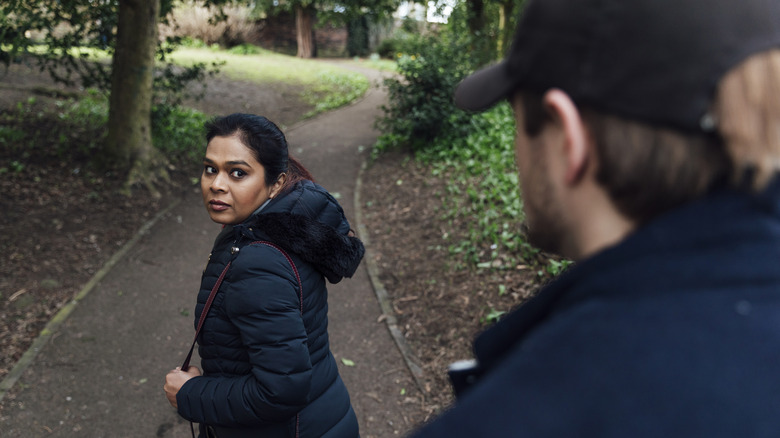 a man stalking a woman near a forested road