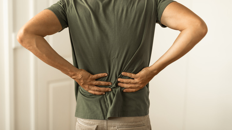 A man in a green T-shirt feels his lower back.