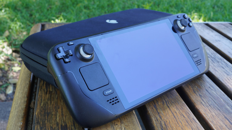 Steam Deck handheld gaming PC resting on its carrying case on an outdoor wooden table.