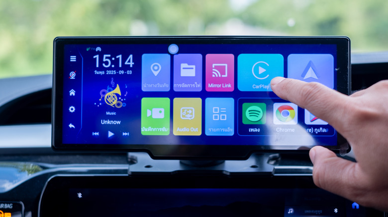A hand reaching toward the CarPlay button on a vehicle's infotainment display
