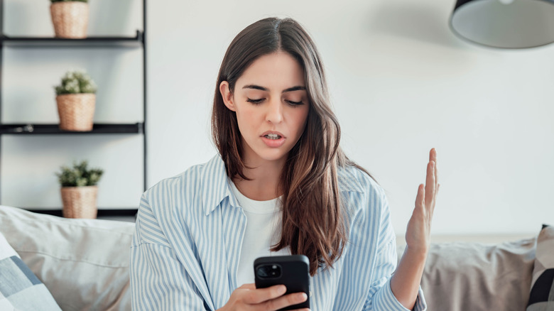 A woman raising a hand in frustrated confusion as she looks at her phone screen