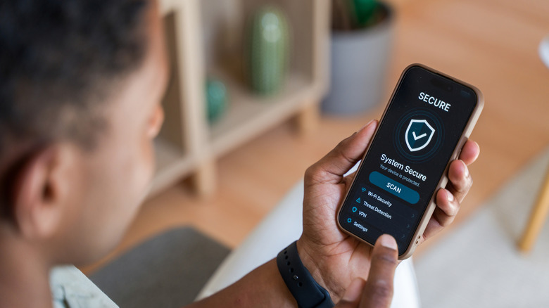 A person looking at their phone showing a shield symbol with the words 'System Secure' on the screen