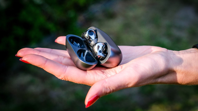 The palm of a hand holding a pair of Huawei FreeBuds in their charging case.