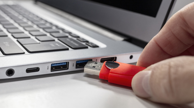A person plugging a USB cable into a blue USB port on a laptop