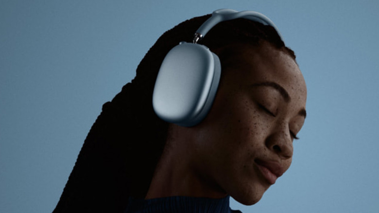 A woman wearing a pair of the Apple AirPods Max 2, set against a pale blue backdrop.