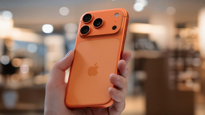 hand holding iphone 17 pro in cosmic orange, blurred background