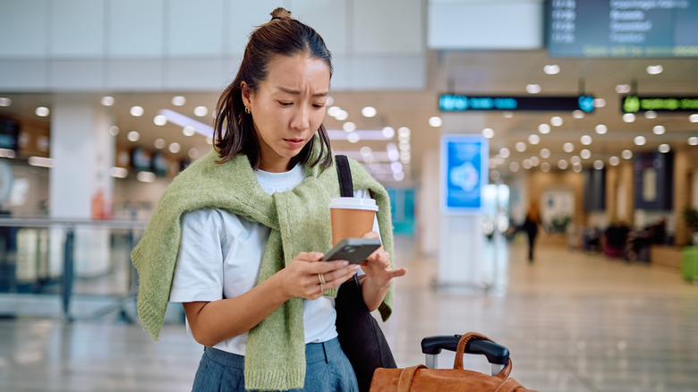 A woman looking worried as she checks her phone in the middle of an airport