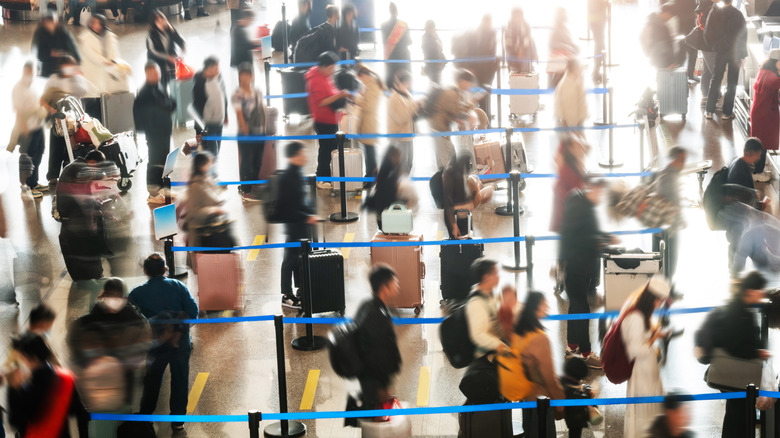 A blurred crowd of people waiting in line to check in at an airport