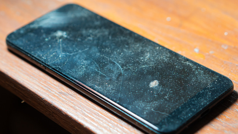 A close up view of a smartphone with a cracked screen lying ontop of a wooden table