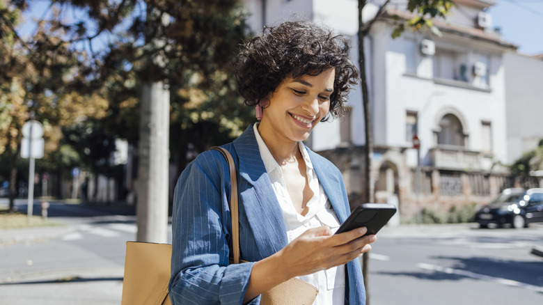 A woman walking down the street and smiling while looking at her phone