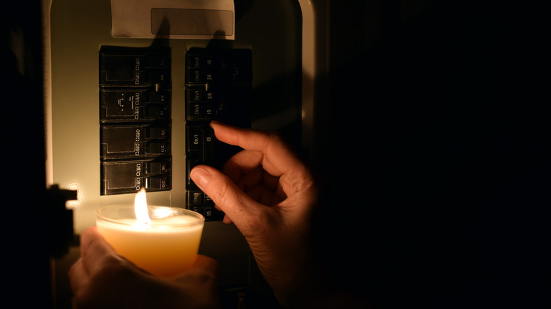 a hand holding a candle up near an electrical control box for a house