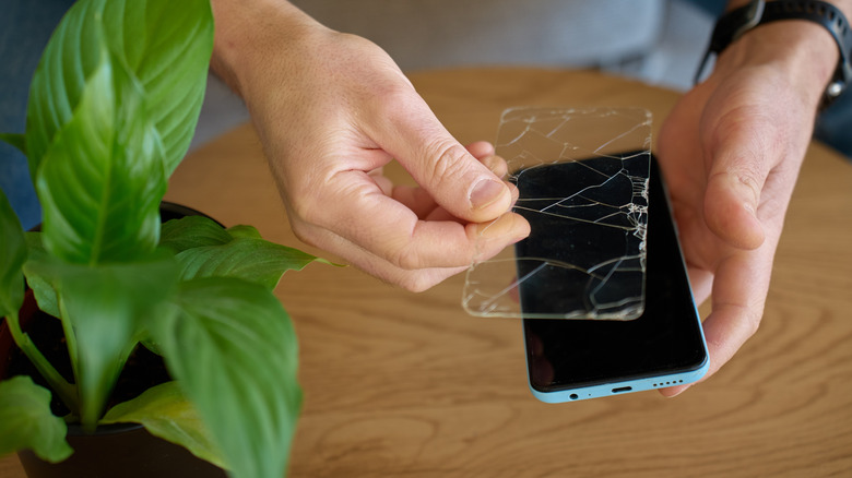 a person removing a broken screen protector from their smartphone