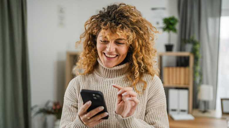 A woman happily using her phone at home