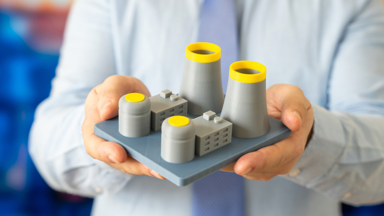 Hands holding a small model of a nuclear power plant